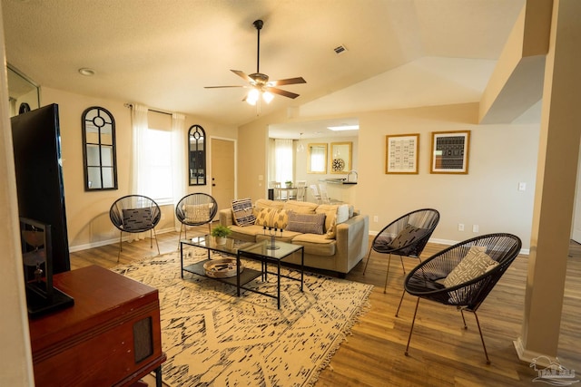 living area featuring visible vents, wood finished floors, baseboards, a ceiling fan, and vaulted ceiling