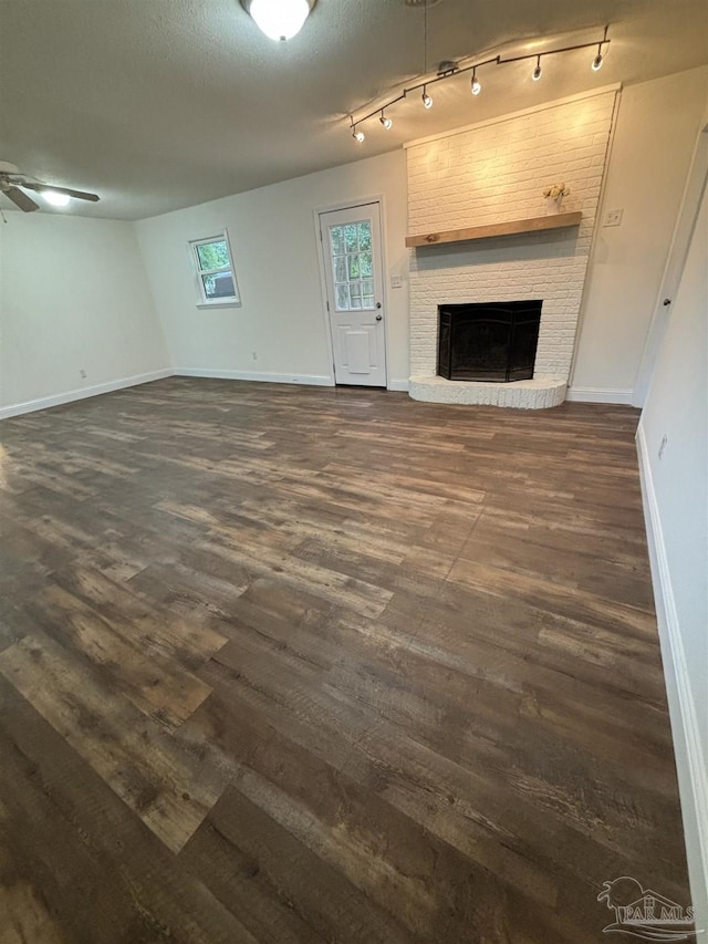 unfurnished living room featuring a brick fireplace, dark hardwood / wood-style floors, a textured ceiling, and ceiling fan