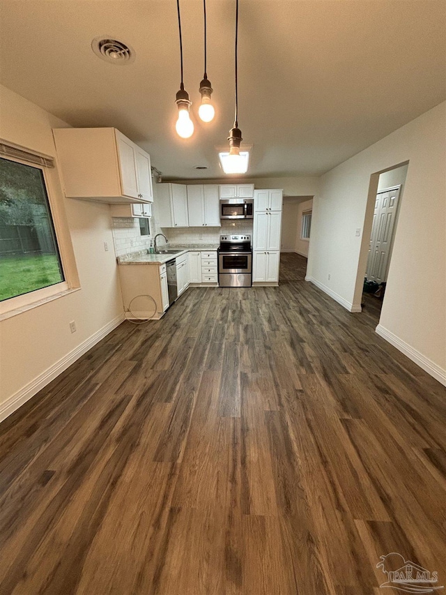 kitchen with tasteful backsplash, appliances with stainless steel finishes, dark hardwood / wood-style floors, pendant lighting, and white cabinets