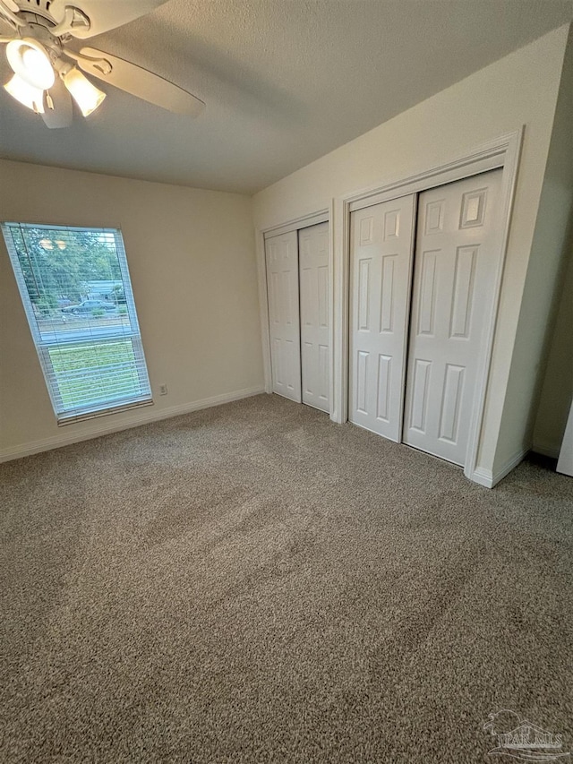 unfurnished bedroom with carpet floors, two closets, a textured ceiling, and ceiling fan