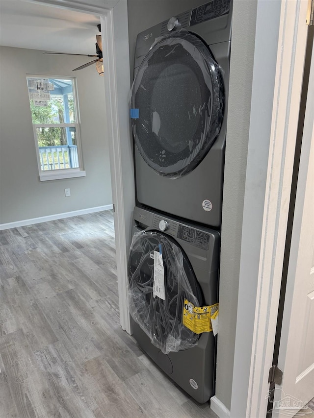 laundry room with ceiling fan, stacked washer and clothes dryer, and light hardwood / wood-style flooring