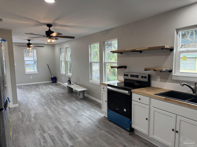 kitchen featuring butcher block countertops, white cabinetry, sink, stainless steel range with electric stovetop, and light wood-type flooring