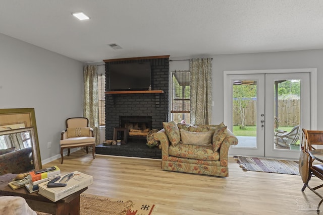 living room with wood finished floors, french doors, visible vents, and a brick fireplace