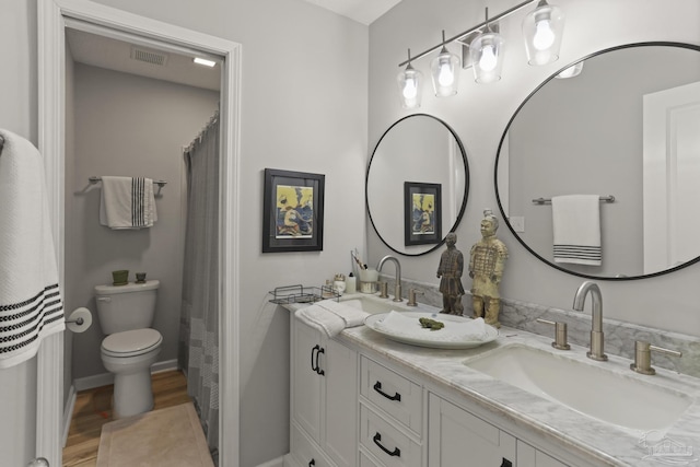 full bath with toilet, wood finished floors, a sink, and double vanity