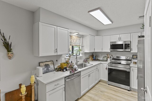 kitchen featuring a sink, light wood-style floors, light countertops, white cabinets, and appliances with stainless steel finishes