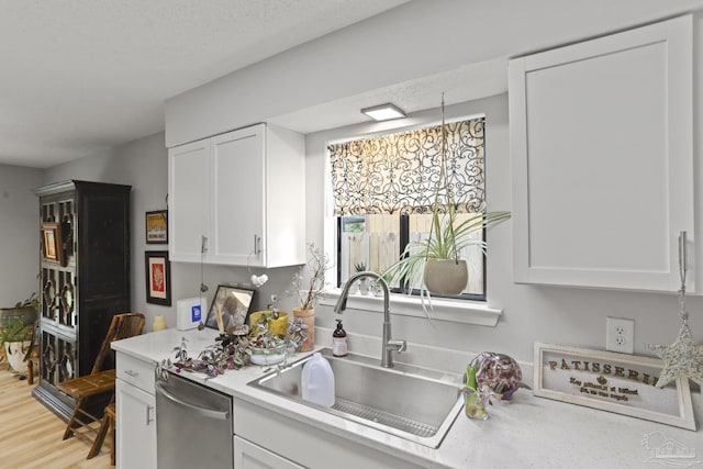kitchen with a sink, light countertops, dishwasher, light wood-style flooring, and white cabinets