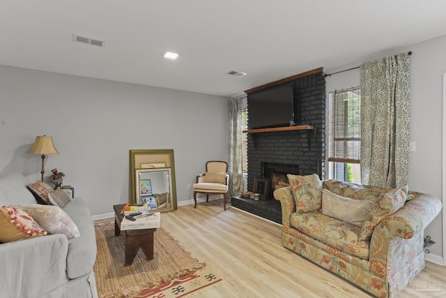 living room with baseboards, wood finished floors, visible vents, and a brick fireplace