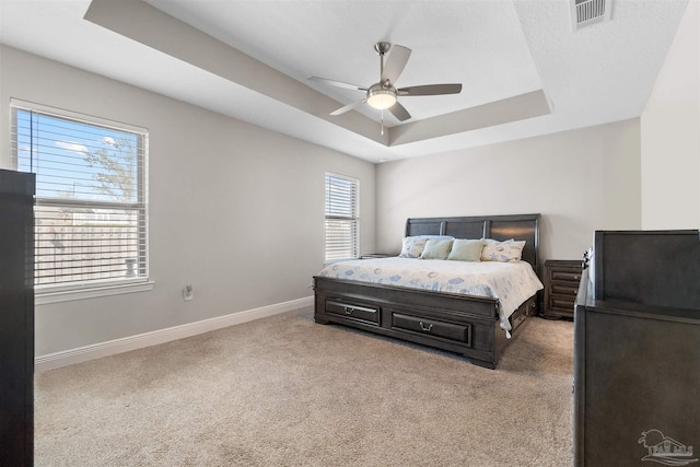 bedroom with light carpet, ceiling fan, and a tray ceiling