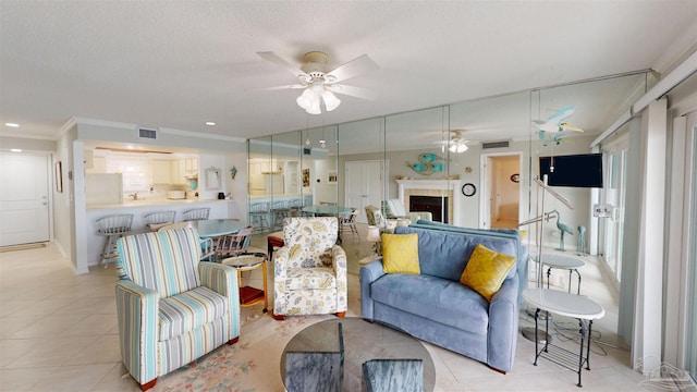 living area featuring light tile patterned flooring, a textured ceiling, visible vents, ornamental molding, and a ceiling fan