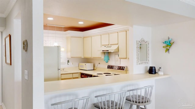 kitchen with recessed lighting, white appliances, under cabinet range hood, a breakfast bar, and a sink