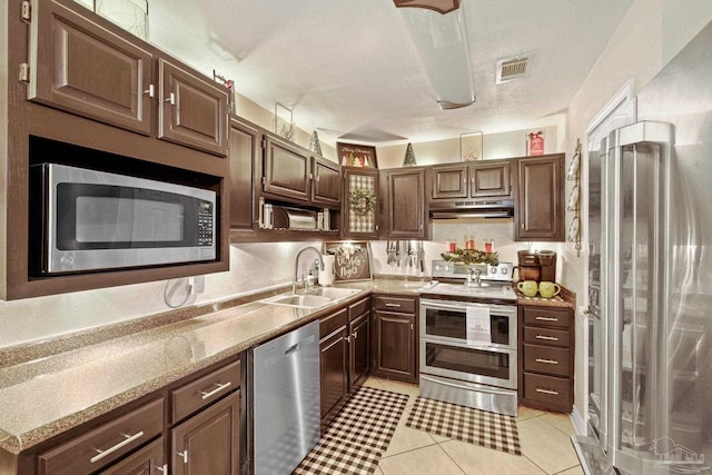 kitchen with dark brown cabinets, sink, light tile patterned floors, and stainless steel appliances