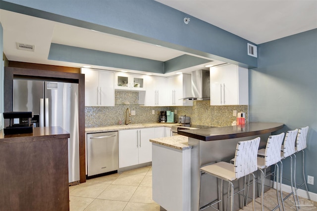 kitchen with white cabinetry, a kitchen breakfast bar, kitchen peninsula, stainless steel appliances, and wall chimney range hood