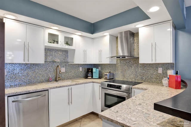 kitchen featuring sink, appliances with stainless steel finishes, wall chimney range hood, light stone countertops, and white cabinets