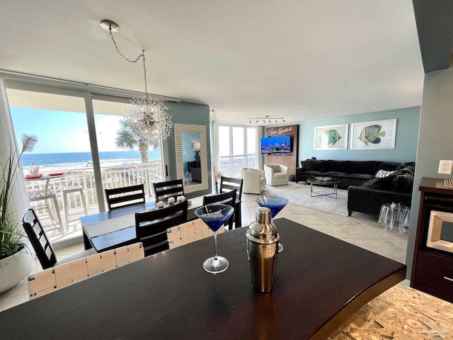 tiled dining room featuring a notable chandelier, floor to ceiling windows, a beach view, and a water view