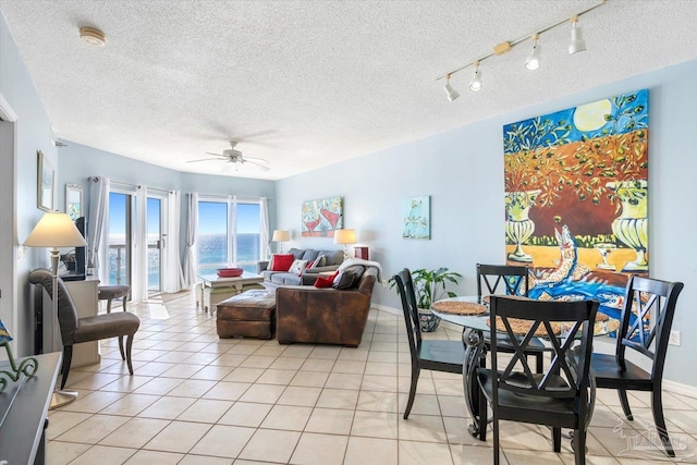 living room featuring a textured ceiling, a water view, light tile patterned floors, and ceiling fan