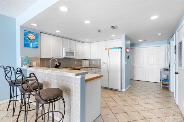 kitchen with kitchen peninsula, white cabinetry, a kitchen bar, and white appliances