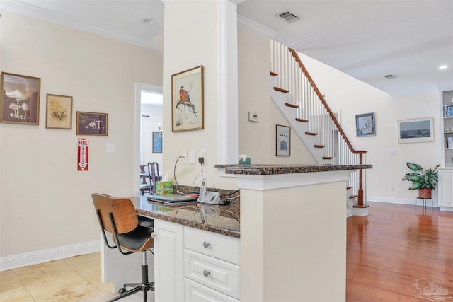 interior space featuring built in desk, white cabinetry, dark stone counters, ornamental molding, and kitchen peninsula