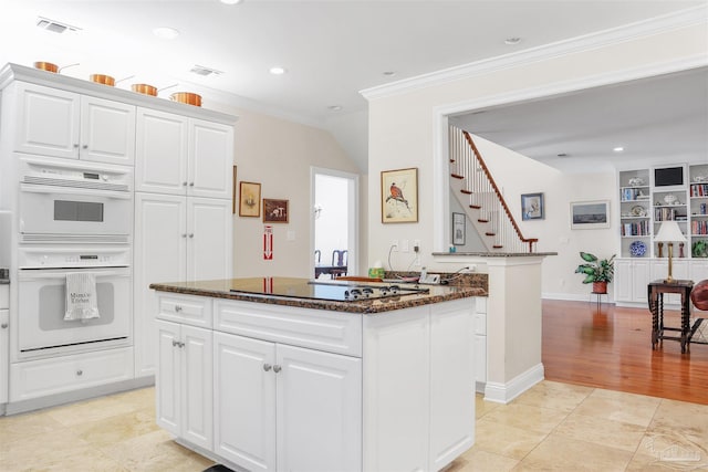 kitchen featuring white cabinetry, a center island, electric stovetop, double oven, and dark stone counters