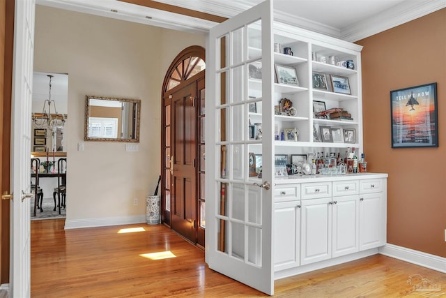 bar with crown molding, light hardwood / wood-style flooring, and white cabinets