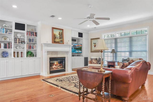 living room with light hardwood / wood-style flooring, a tile fireplace, ceiling fan, ornamental molding, and built in shelves