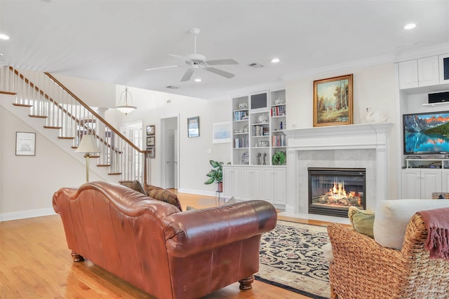 living room with built in shelves, ornamental molding, a tile fireplace, and light wood-type flooring