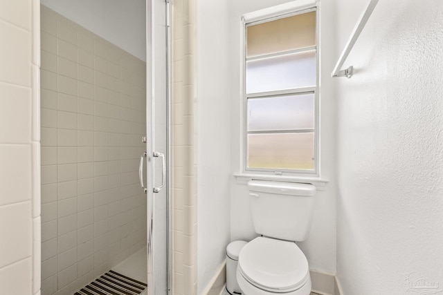 bathroom featuring a shower with door and toilet