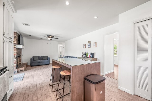 kitchen with light hardwood / wood-style flooring, white cabinets, ceiling fan, and a center island