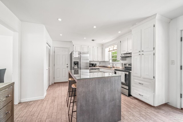 kitchen featuring a breakfast bar, white cabinets, a kitchen island, light hardwood / wood-style flooring, and appliances with stainless steel finishes