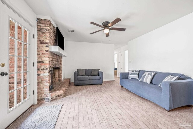 living room featuring ceiling fan, a brick fireplace, light hardwood / wood-style floors, and a wealth of natural light