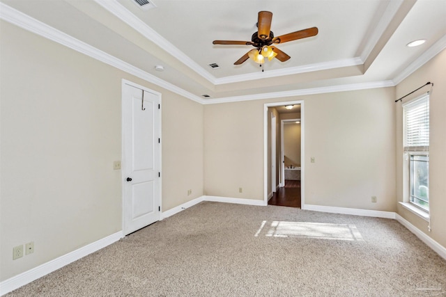 empty room with ceiling fan, a raised ceiling, ornamental molding, and carpet