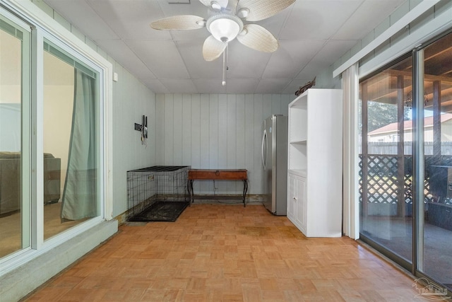 interior space with ceiling fan, light parquet flooring, wooden walls, and a paneled ceiling