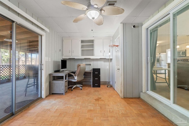 office space featuring light parquet floors, ceiling fan, and wood walls