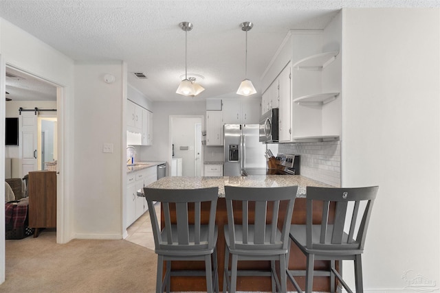 kitchen with appliances with stainless steel finishes, white cabinets, light colored carpet, kitchen peninsula, and a barn door