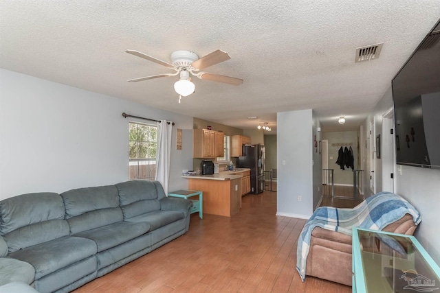 living room featuring ceiling fan, a textured ceiling, and light hardwood / wood-style floors