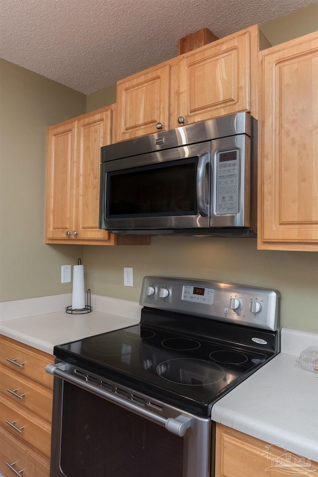 kitchen featuring light brown cabinets, a textured ceiling, and stainless steel appliances