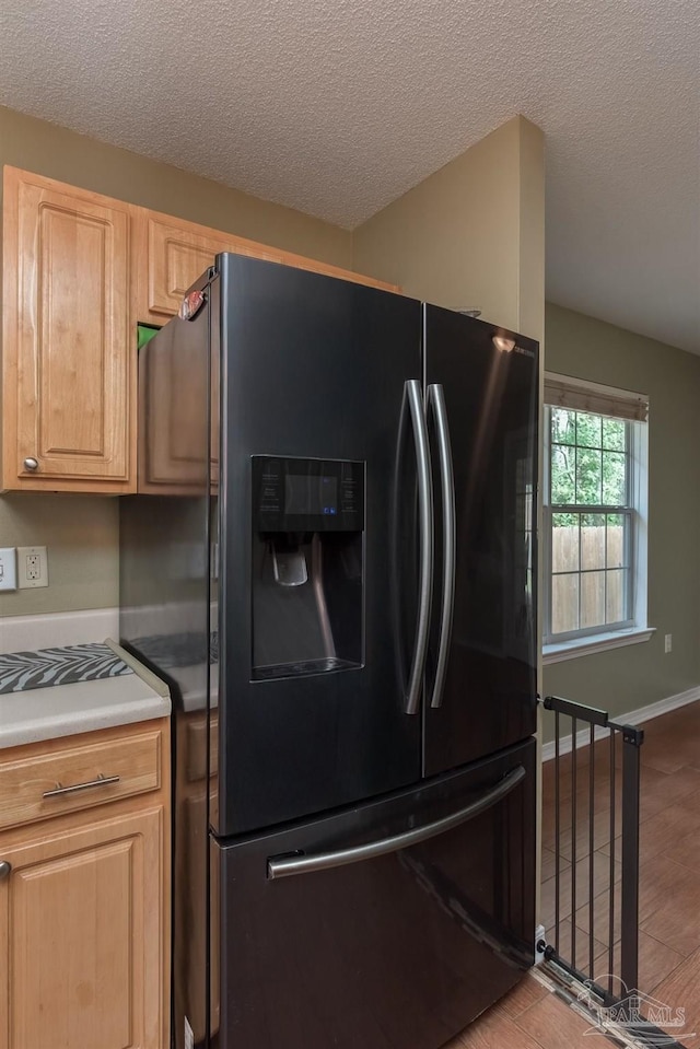 kitchen with light brown cabinetry, light hardwood / wood-style floors, a textured ceiling, and black fridge