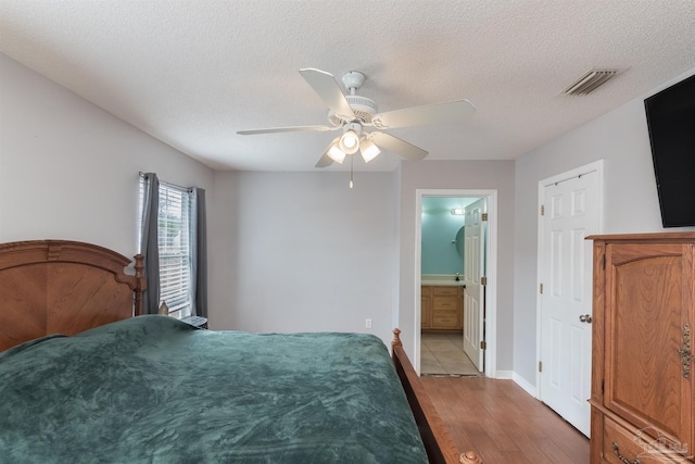 bedroom with ceiling fan, a textured ceiling, light hardwood / wood-style floors, and ensuite bath