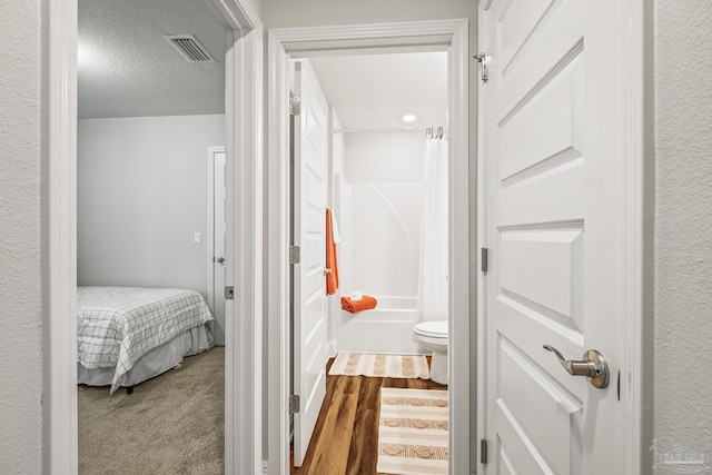 interior space with toilet, a textured ceiling, and shower / tub combo with curtain