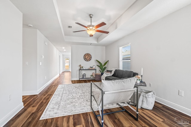 living room featuring a raised ceiling, ceiling fan, and dark wood-type flooring