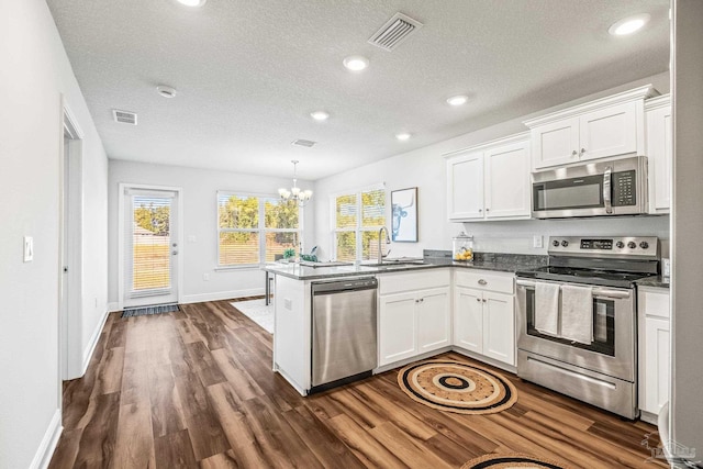 kitchen with pendant lighting, an inviting chandelier, white cabinets, appliances with stainless steel finishes, and kitchen peninsula