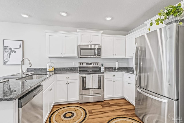 kitchen featuring white cabinetry, sink, stainless steel appliances, dark stone counters, and light hardwood / wood-style floors