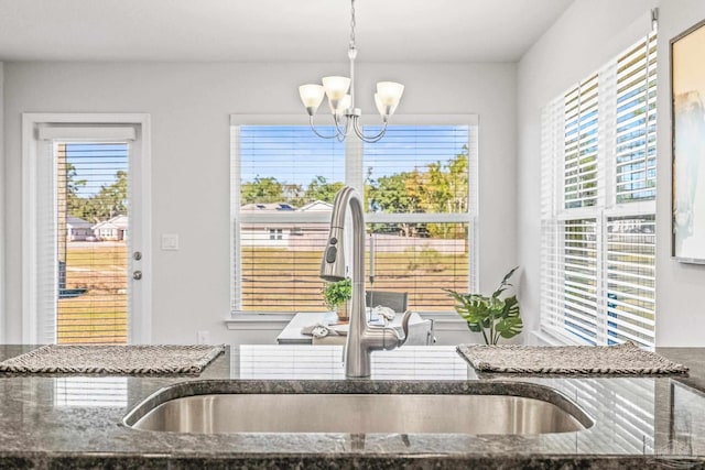 kitchen with dark stone counters, sink, pendant lighting, a chandelier, and plenty of natural light