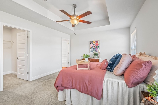 bedroom featuring ceiling fan, a spacious closet, light carpet, and a tray ceiling