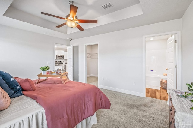 bedroom with a raised ceiling, a spacious closet, ceiling fan, and ensuite bathroom