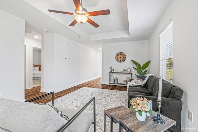 living room featuring hardwood / wood-style floors, a raised ceiling, and ceiling fan