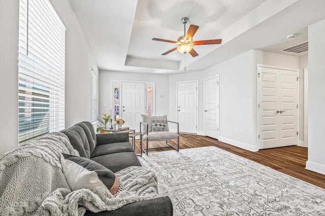 living room featuring dark hardwood / wood-style flooring, ceiling fan, and a raised ceiling