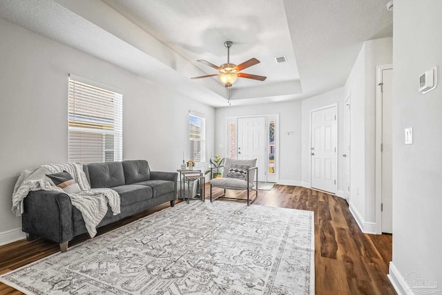 living room with a tray ceiling, ceiling fan, and dark wood-type flooring