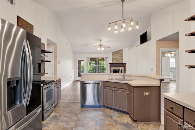 kitchen featuring dark brown cabinets, a stone fireplace, stainless steel appliances, pendant lighting, and sink