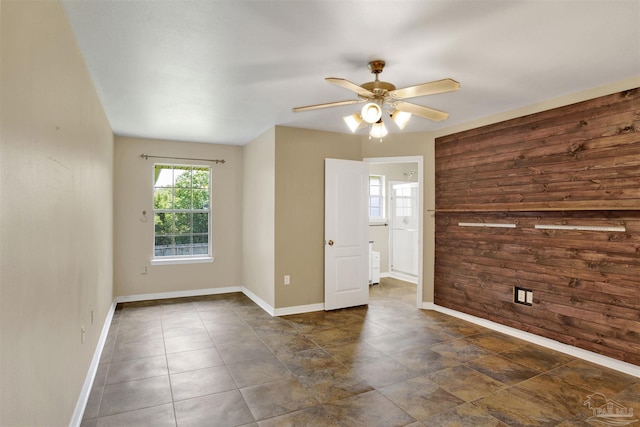 spare room featuring ceiling fan and wooden walls