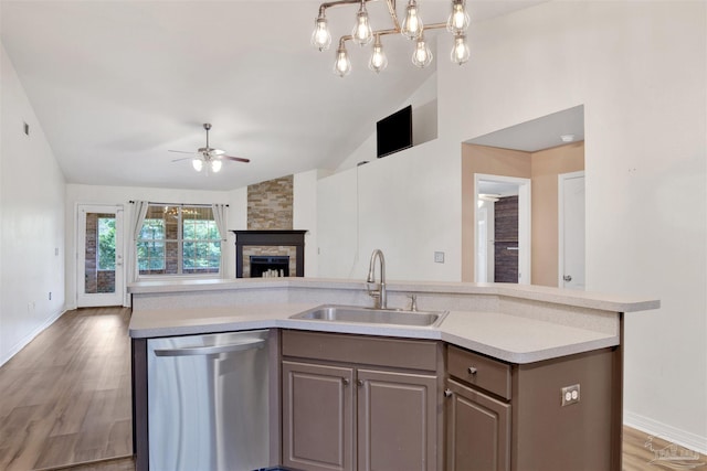 kitchen with wood-type flooring, a stone fireplace, stainless steel dishwasher, sink, and a kitchen island with sink